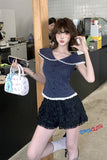Woman holding a handbag in an indoor setting, wearing a navy blue top and black skirt.