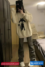 Person wearing a white sweater with a black cat design in a room.