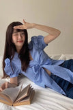 Woman in a blue checkered outfit lying on a bed with an open book