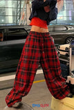 Person wearing red plaid pants and a black top in an urban setting with cars and luggage.