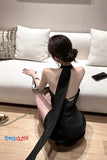 Woman in a black dress sitting on the floor with a phone and handbag nearby, brand 'TOMS CLOTH' visible.