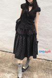 Person wearing a black polka dot dress with a vest against a textured wall.