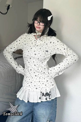 Person wearing a white blouse with star patterns and blue jeans indoors.