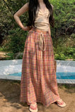 Person wearing a plaid skirt and beige top outdoors by a pool.