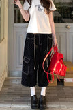 Person wearing a white t-shirt with a graphic design, black polka dot pants, and holding a red bag.