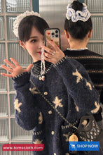 Woman taking a mirror selfie wearing a dark blue sweater with white patterns, holding a phone with a visible brand logo.