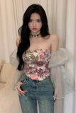 Woman wearing a floral top and jeans with sheer sleeves against a beige curtain background