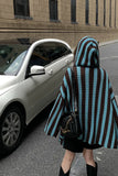 Person wearing a striped poncho walking on a street with a car in the background