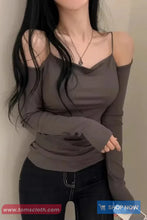 Woman wearing a gray long-sleeve top with cut-out shoulders against a plain background.