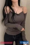 Woman wearing a gray long-sleeve top with cut-out shoulders against a plain background.