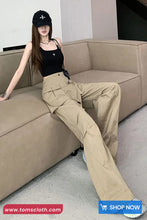 Woman sitting on a beige couch wearing a black cap, black top, and beige pants with 'www.tomscloth.com' branding.