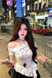 Woman in a white off-shoulder top standing on a city street at night.