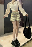 Person wearing a white blouse, striped shorts, and black shoes holding a black bag.