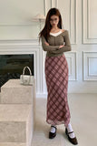 Woman in a plaid skirt and green top standing in a room with a fireplace.