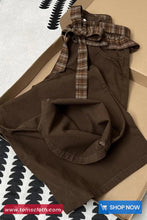 Brown dress with plaid ruffled collar on a patterned surface, brand 'Toms Cloth' visible.