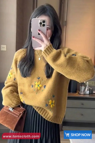 Person wearing a yellow sweater with floral patterns, taking a mirror selfie.