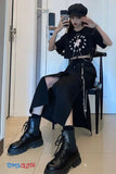 Person wearing a black outfit with a floral top, high-waisted pants, and black boots, sitting on a chair.