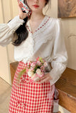 Woman holding flowers, wearing a white lace blouse and red checkered skirt.