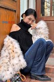 Woman sitting on steps wearing a black turtleneck and blue jeans, with a fur coat draped over her shoulders.