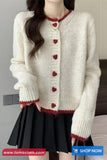White cardigan with red heart buttons worn by a person, with a gray background.