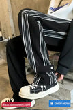 Person wearing black and white striped pants with a black jacket and white sneakers.