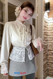 Woman wearing a white blouse with lace details and a gray skirt, standing indoors.
