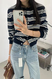 Person wearing a striped sweater and jeans, holding a phone, with a white background.
