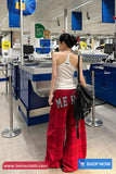 Woman in a checkout area of a store, wearing a white tank top and red plaid pants with 'MER' on them.