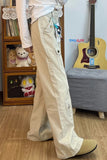 Person wearing beige pants with a white shirt in a room with a guitar and shelves.