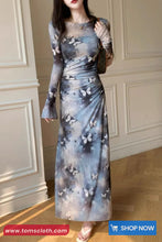 Woman wearing a long, floral-patterned dress against a neutral wall.