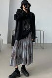 Person wearing a black outfit with a long, patterned skirt in a minimalistic room.