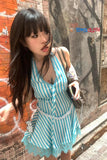 Woman in a blue and white striped dress standing against a brick wall with a visible brand logo.