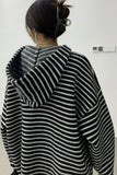 Person wearing a black and white striped sweater with a hood against a plain background