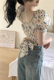 Woman wearing a floral blouse and denim skirt in a room.