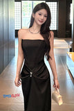 Woman in a black dress holding a beige handbag indoors