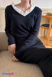 Person wearing a navy sweater with white ruffled collar sitting on a couch.