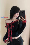 Woman wearing a black off-shoulder top with red plaid accents, holding a phone.