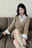 Woman wearing a beige sweater dress and white shirt sitting on a couch.
