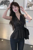 Woman wearing a black top and dark jeans, posing indoors with a blurred background.