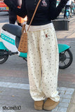 Person wearing a black top and white polka dot pants with a brown bag on a street.