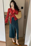 Person wearing a red floral blouse and blue denim skirt, holding a beige bag, taking a mirror selfie.