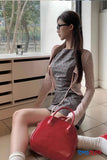 Woman sitting on a windowsill holding a red handbag, wearing sunglasses and a patterned dress.