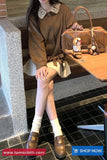 Person sitting on a bench with a brown handbag, wearing a brown outfit and white shoes.
