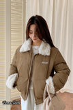Woman wearing a brown puffer jacket with white fur trim indoors.