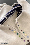 Close-up of a white sweater with colorful buttons and a striped collar.