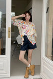 Woman in a floral shirt and shorts standing in a doorway.