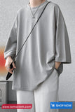 Person wearing a gray oversized shirt and white pants against a gray background with 'tomscloth.com' branding.
