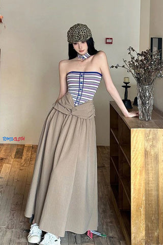 Woman in a striped top and beige skirt standing in a room with wooden furniture.