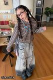 Person wearing a textured gray hoodie and ripped jeans in a room with wooden floor and furniture.