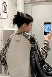 Person taking a mirror selfie wearing a camouflage-patterned shirt with a logo.